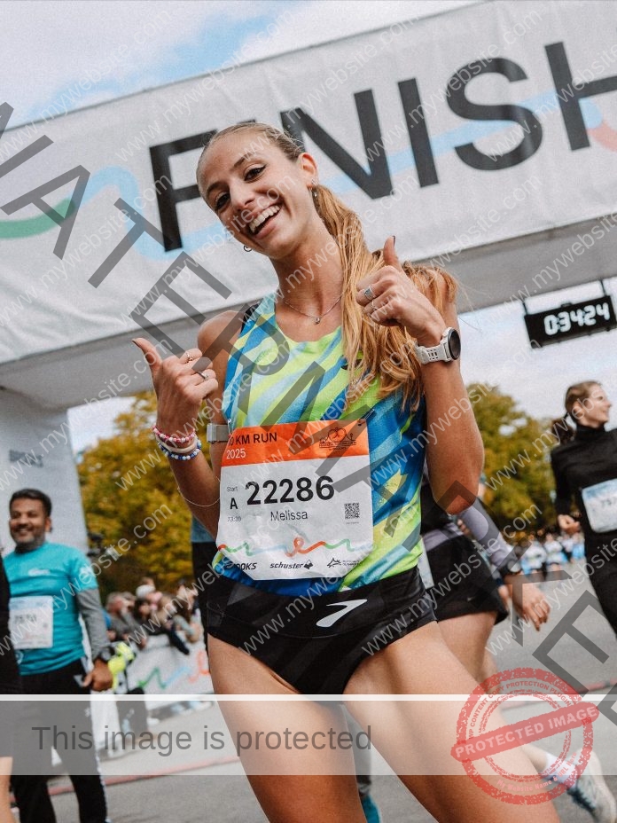 Melissa Fracassini, a smiling female runner, gives two thumbs up at a race finish line in a colorful tank and bib 22286.