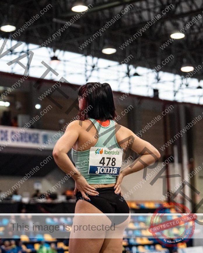 Olga Guerra stands hands on hips, facing away in an indoor stadium, wearing sportswear and bib 478, ready to race.