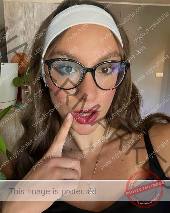 Paulinka Kubis posing for a photo with red lipstick, a white headband, glasses and her pointer finger to the side of her mouth