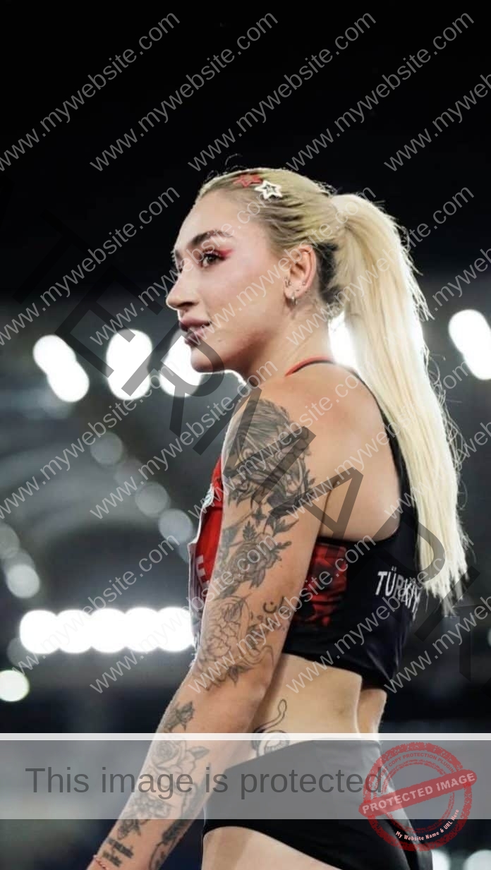 Tugba Dansmz, a Turkish athlete with blonde hair in a ponytail and arm tattoos, stands in an arena under bright stadium lights.