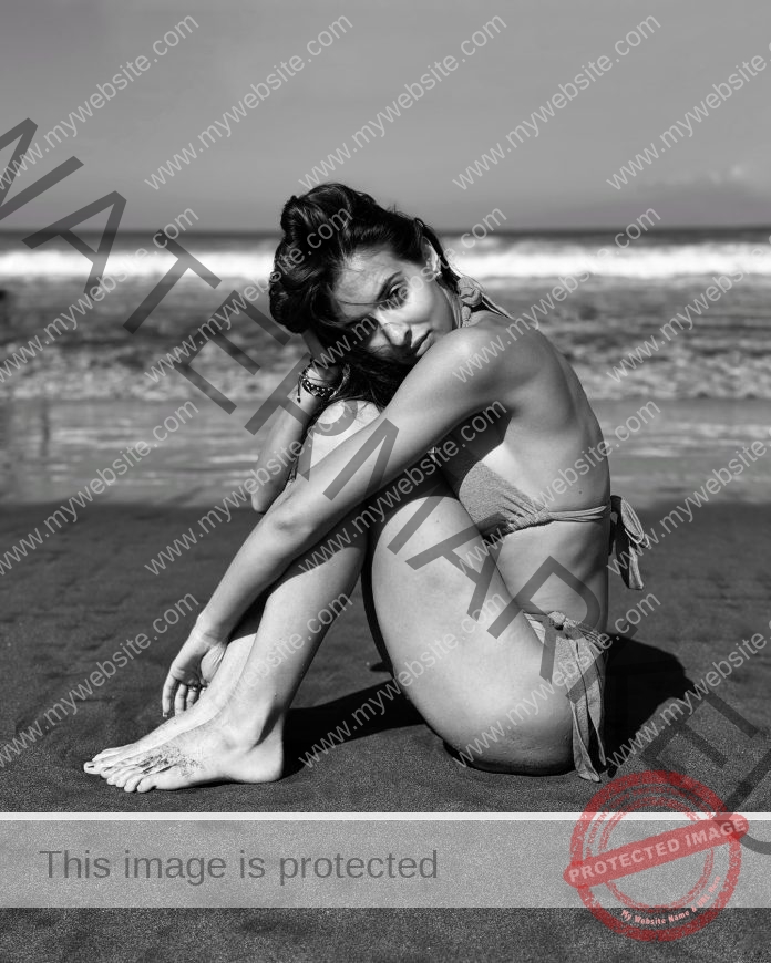 Vodnyánszká Renáta sitting on the beach in a bikini, knees pulled up to her face, in black and white.