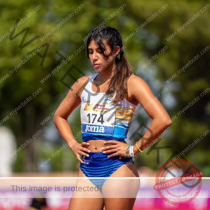 Nicole Barrios waits for her race to start with her hands on her hips wearing a blue and white track uniform.