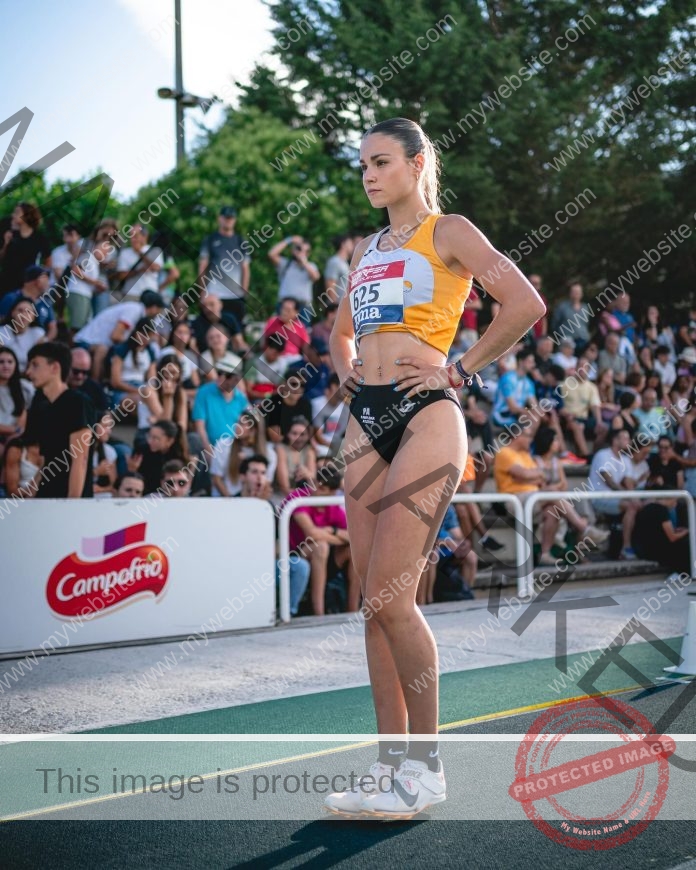 Andrea Arilla prepares to compete on a sunny track before a cheering crowd and green backdrop.