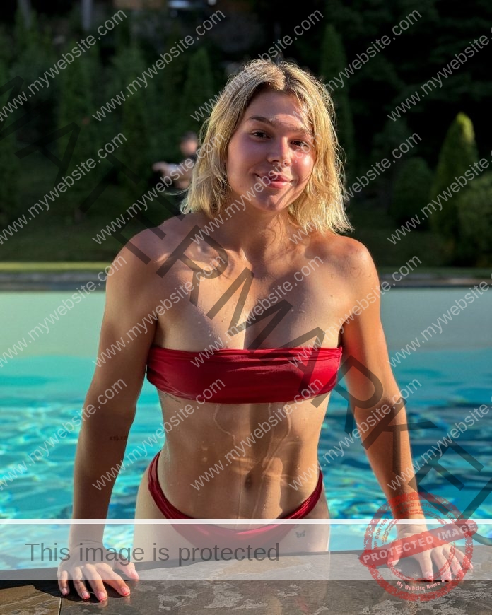 Anisiya Lochman lifts herself out of the pool wearing a red bikini and smiling at the camera