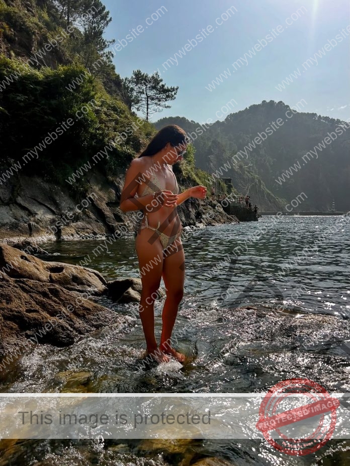 Aracely Martinez standing in a peaceful lake surrounded by sunlit hills and lush greenery.