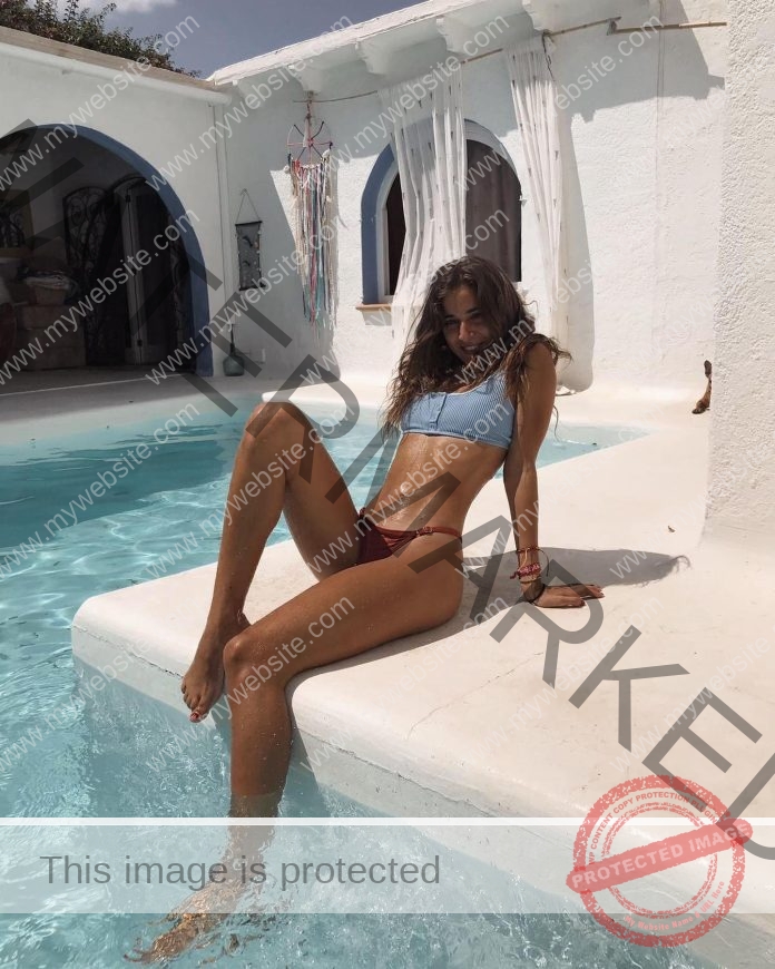 Daniela Garcia lounging poolside, one leg bent and leaning back, wearing a light blue bikini.