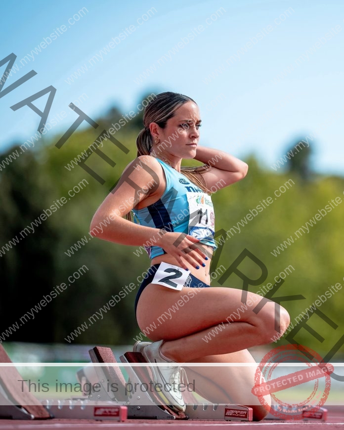 Esperanza Rueda preparing to sprint on a sunny outdoor track with focus and determination.