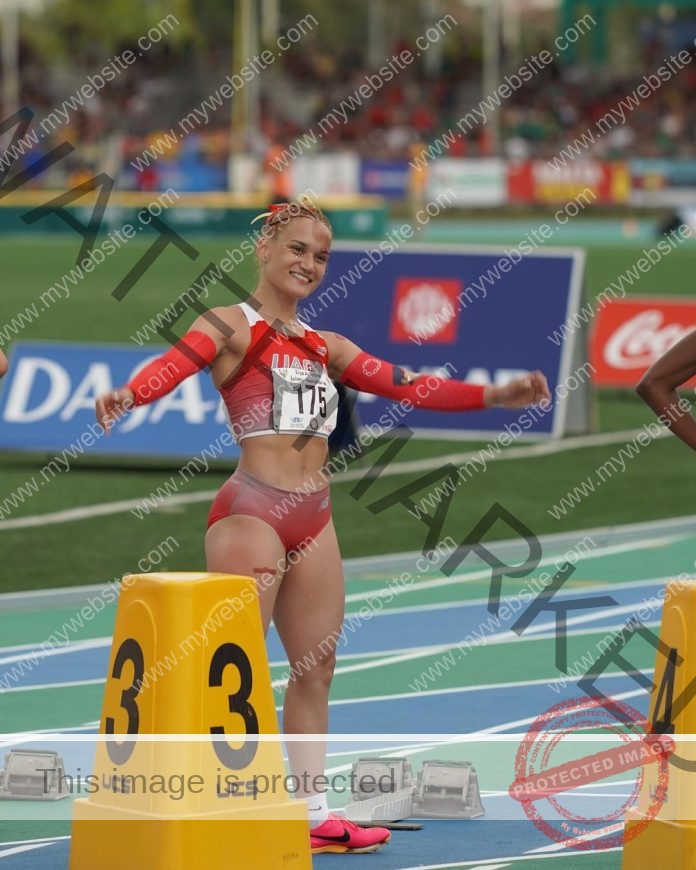 Gladymar Torres smiling at starting blocks before race on blue-lined track in red uniform.