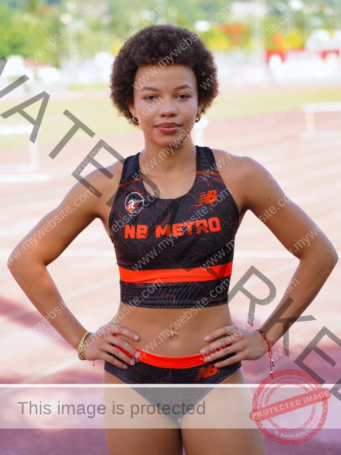 Grace Motero stands confidently on a running track in a black and orange NB METRO uniform, hands on hips, representing Puerto Rico.