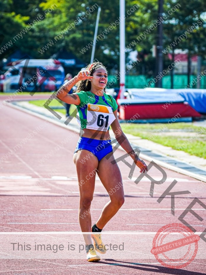 Hakelly de Souza celebrating after finishing a sprint on a sunny outdoor track.
