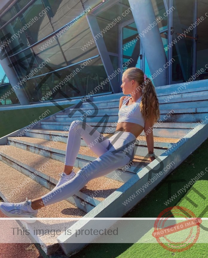 Heidi Salminen sitting on stairs & leaning back, wearing long tights and a crop top.