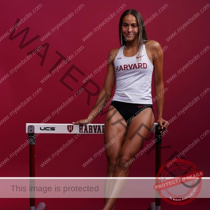 Izzy Goudros, a female athlete in Harvard track gear, stands confidently by a hurdle against a solid maroon background.