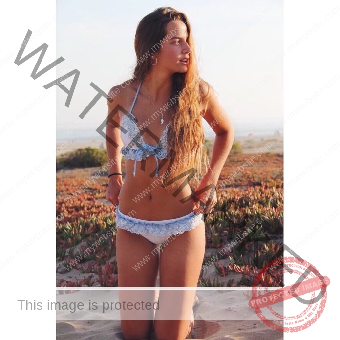 Javi Musalem posing on a sandy beach in a blue bikini under golden summer sunlight.