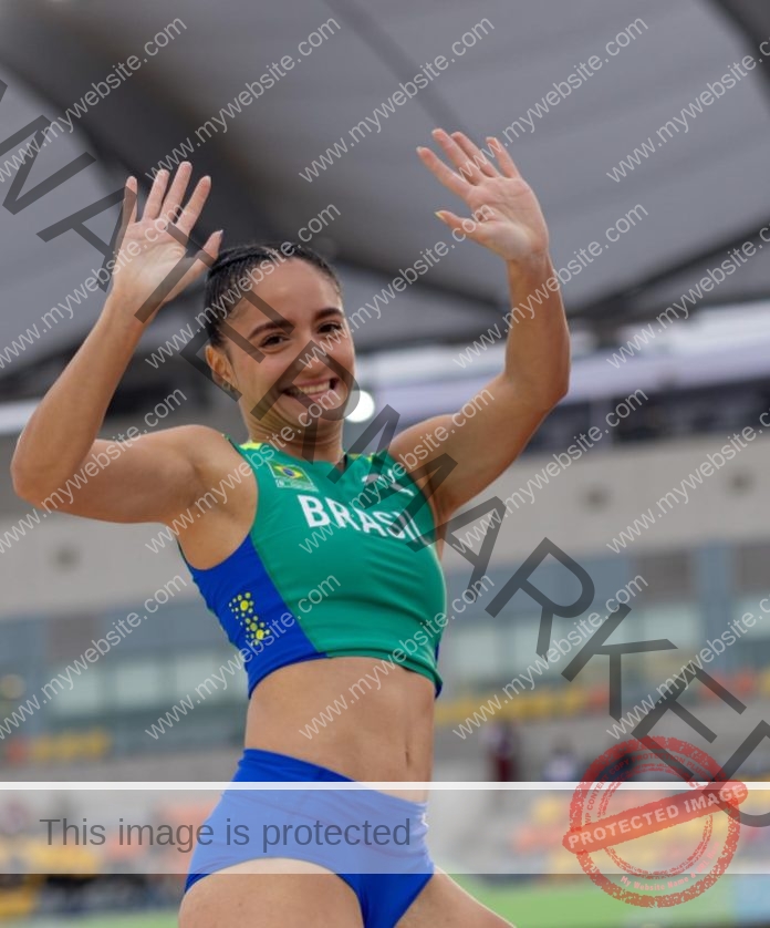 Brazilian sprinter Julia Calabretti celebrates victory with raised arms and a joyful smile on the track.