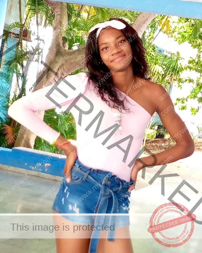 Young woman in pink top and denim shorts smiling in tropical resort setting.
