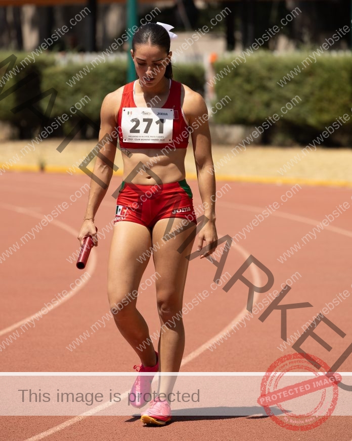 A very fit and muscular Mariana Goncedo holding a baton and preparing for a relay in her blood-red Mexican track top and bottom.