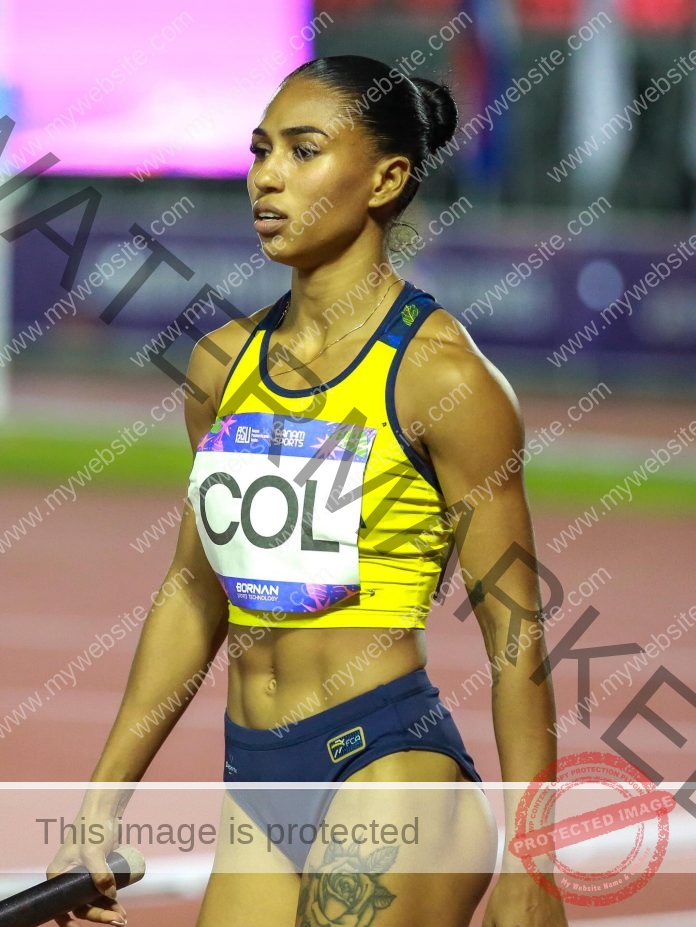 Marleth Ospino holds the baton, ready to begin the 4x100m relay for the Colombia national team, in her yellow and navy track uniform.