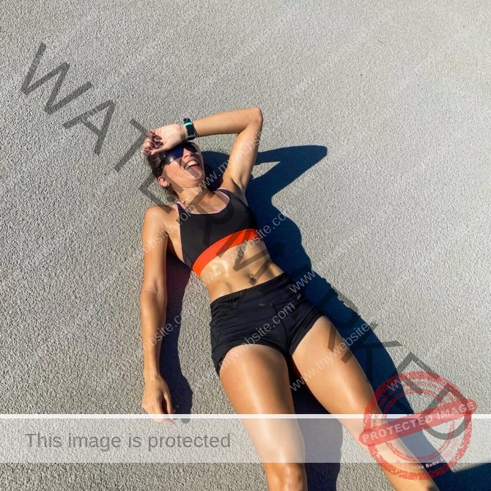 Micaela González lying on the track looking exhausted, wearing a black and red track uniform.