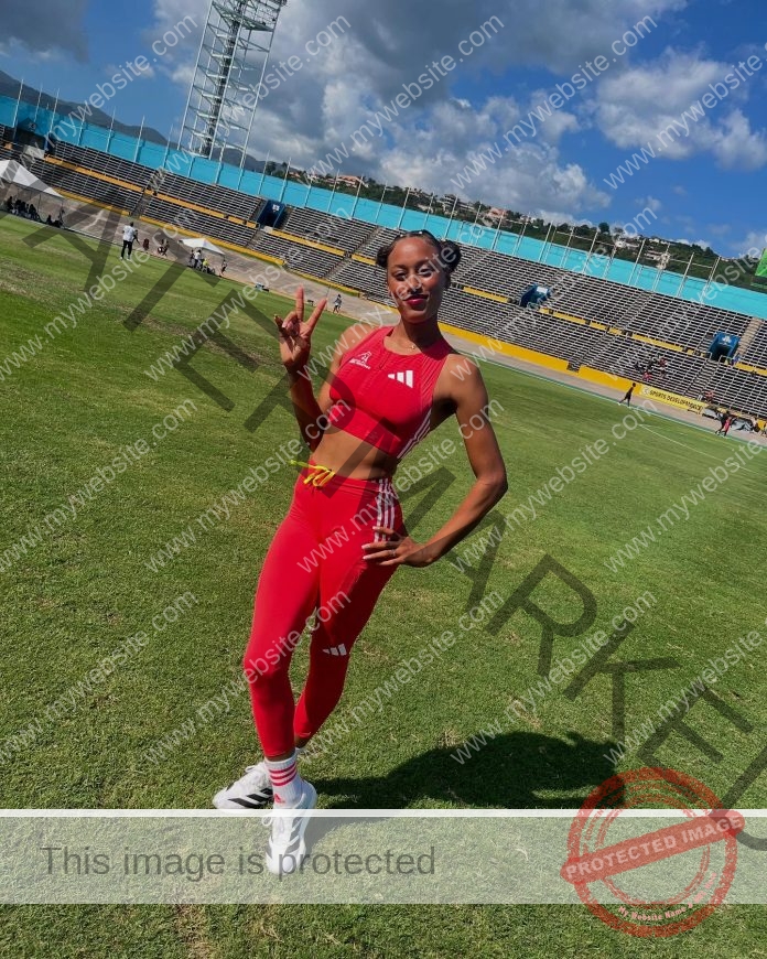 Micheiry Brito posing on a green track field in a red athletic outfit, smiling confidently.