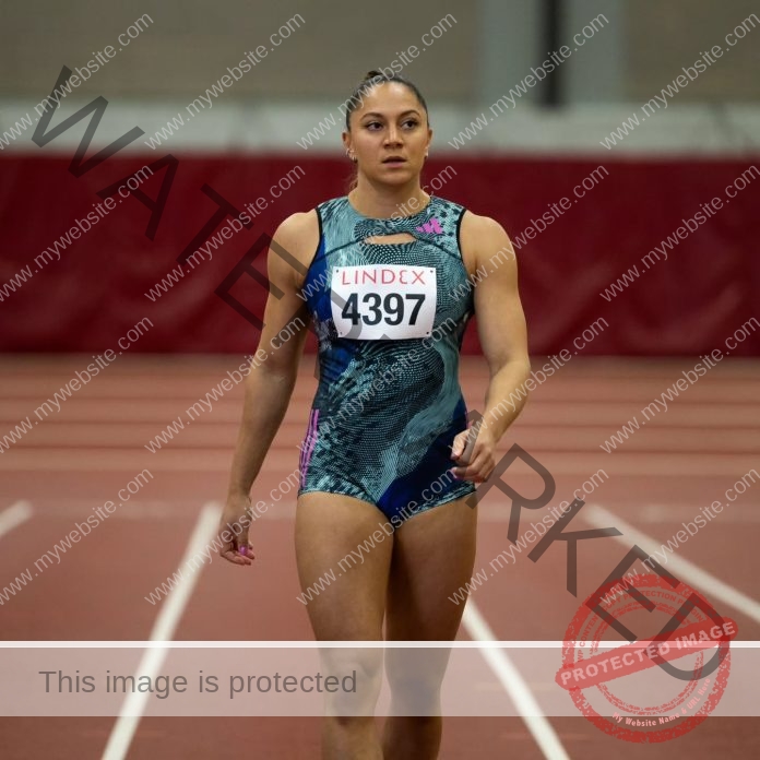Naomi Sedney walking confidently on indoor track in blue and green racing suit, preparing to compete.