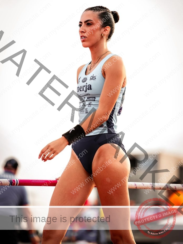 Nerea Pérez Moltó wearing her track suit preparing to pole vault, with intent and focus on her face. There are blurred people in the background.