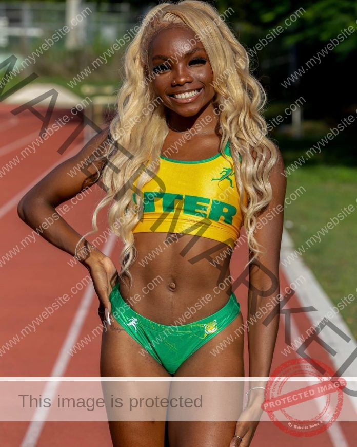 Shary Vallecilla stands confidently on a sunlit running track, smiling in a yellow and green athletic outfit with “INTER” on her top, her blonde hair flowing as she poses with one hand on her hip, radiating energy and athletic confidence.