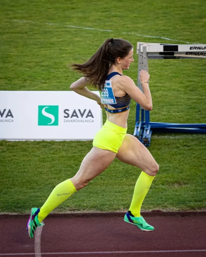 Trisha Mandelc sprinting mid-stride on a grassy outdoor track in vibrant neon yellow shorts.