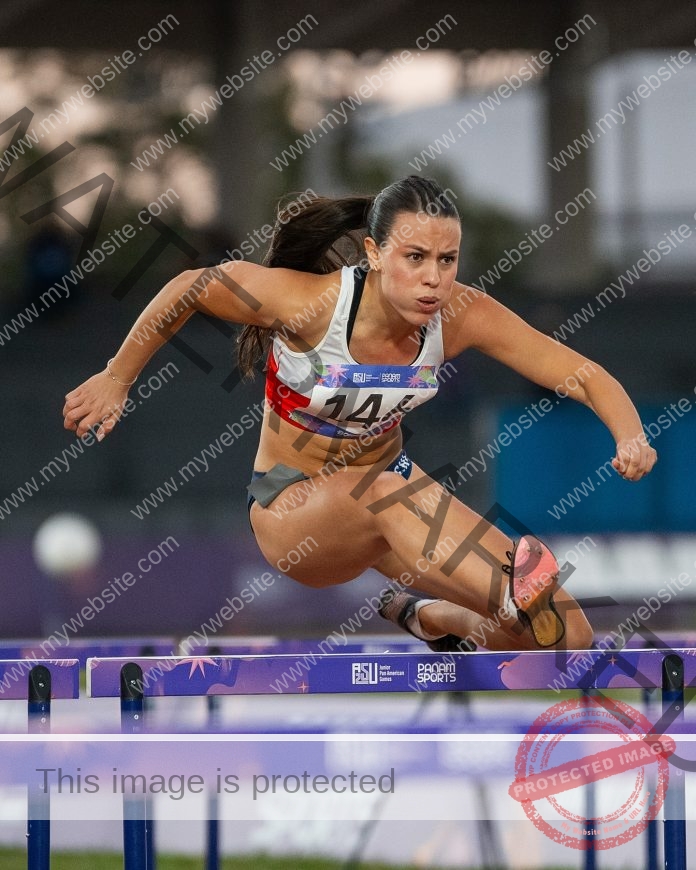 Cata Rozas jumps over a purple hurdle during an outdoor track and field race.
