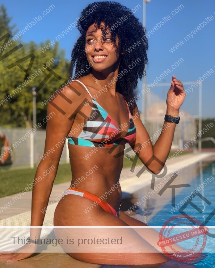 Eliani Casi sitting on the edge of a pool, smiling, with a multi-colored bikini.