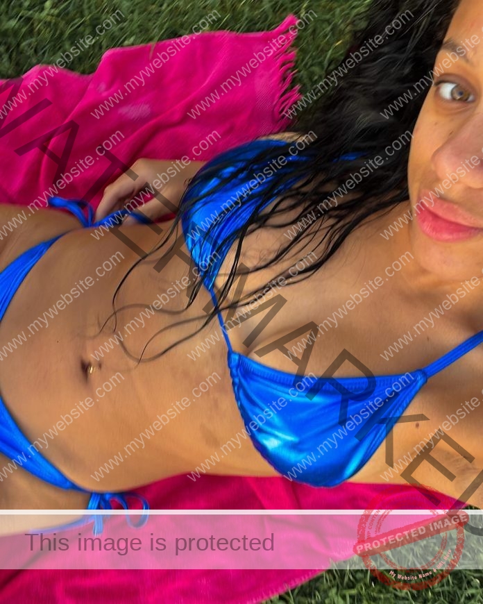 Genesis Capellan posing for a selfie in a very small blue string bikini, smiling at the camera.