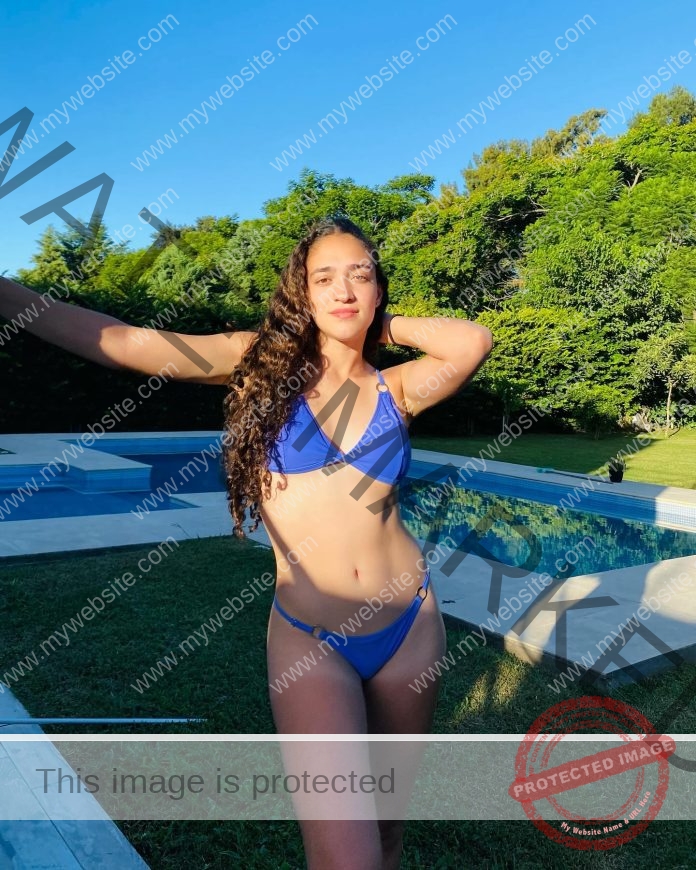 Luli Ferreyra smiling by a sunny pool in Argentina, wearing a blue bikini.