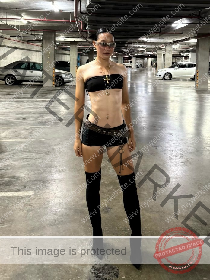 Manatsada Sammano posing confidently in black fashion outfit and boots in urban parking garage.