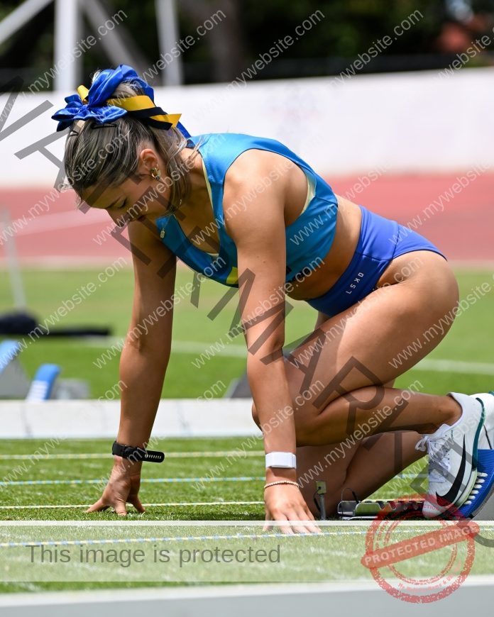 Athlete in blue uniform preparing to sprint on track field.
