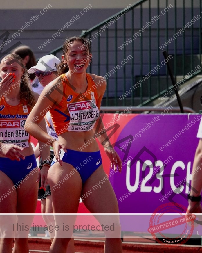 Fenna Achterberg and another female athlete in orange and blue track uniforms celebrate on a track; purple event sign in background.