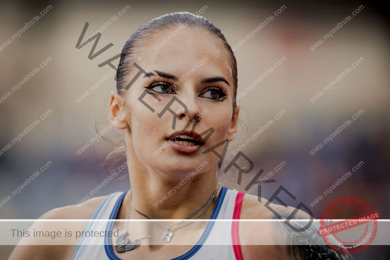 karolina-manasova-czechia-karolina_manasova-344 Karolína Maňasová with slicked-back hair, bold eye makeup, tank top, necklaces, and a shoulder tattoo in a stadium setting.