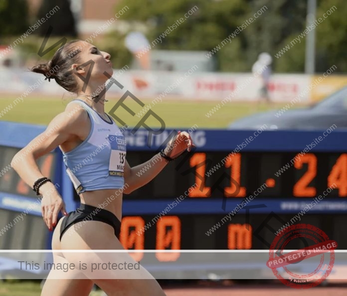 Karolína Maňasová in a light blue top and black shorts crosses the finish line on a track with a timer display showing 11:24.