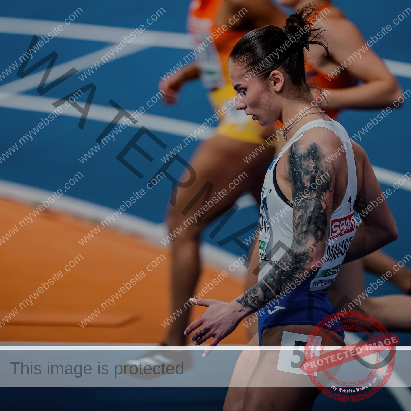 karolina-manasova-czechia-karolina_manasova-380 Karolína Maňasová, a track athlete with visible tattoos and a number 5 bib, sprints indoors as other runners blur in the background.