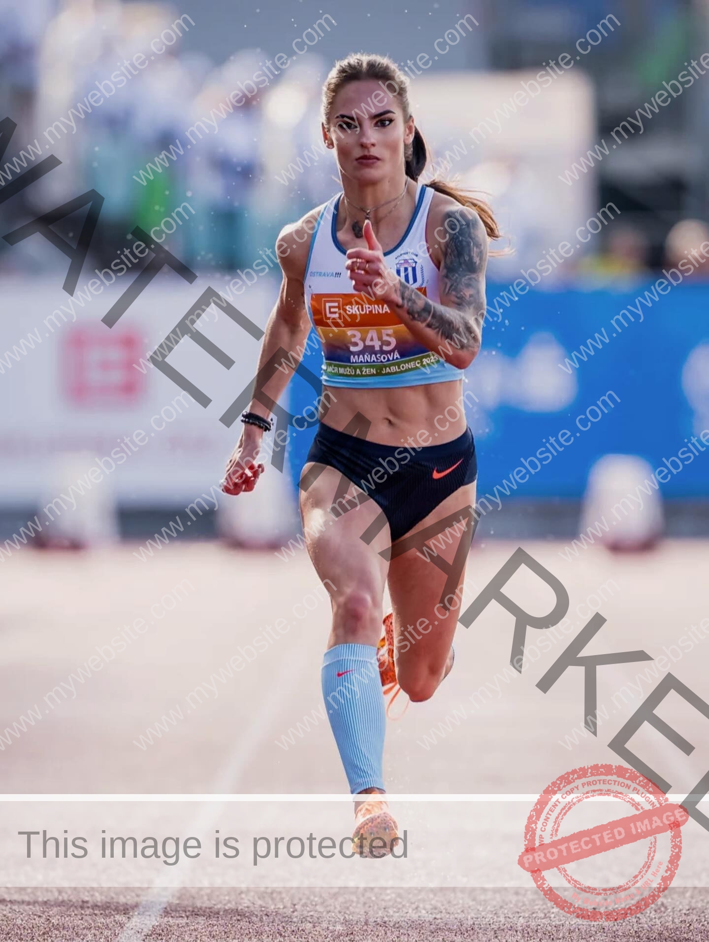 karolina-manasova-czechia-karolina_manasova-387 Karolína Maňasová, focused, sprints on a track in crop top, shorts, compression socks, sporting an arm tattoo and bib 345. Blurred crowd.