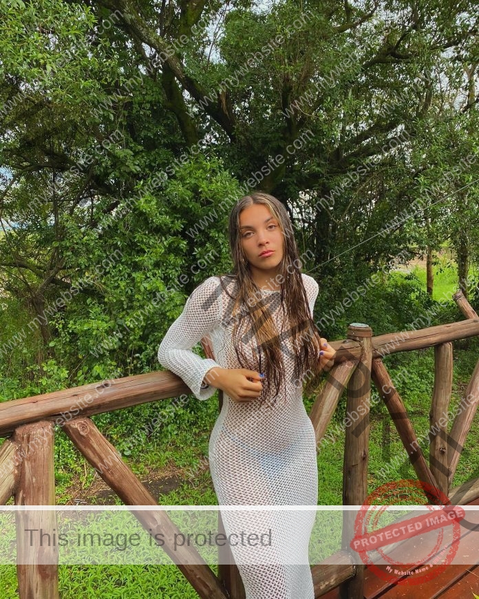 Martina Zunino posing in a white dress on a wooden deck surrounded by lush greenery.