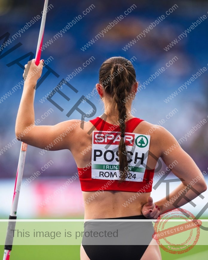 Isabel Posch A female track and field athlete, Isabel Posch of Austria, with a long braid, stands holding a javelin at an event.