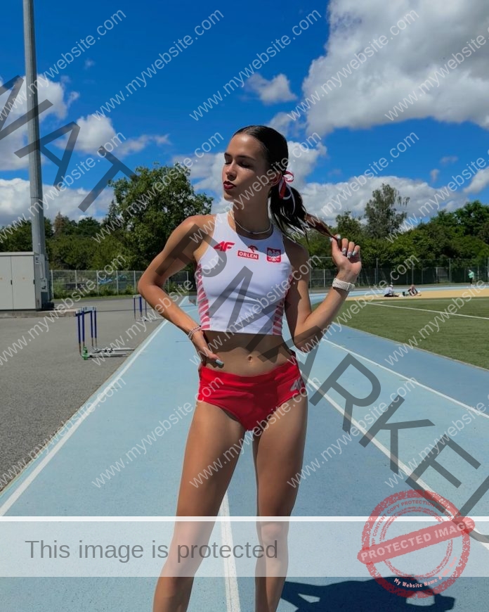 Jagoda Zukowska Jagoda Zukowska, a Polish track athlete, stands on a blue track in red and white, holding her ponytail; hurdles behind.