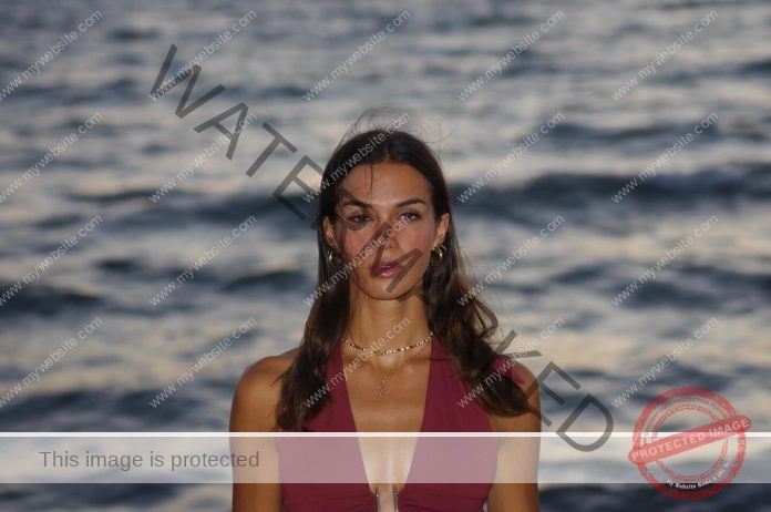 Jagoda Zukowska Jagoda Zukowska, in a maroon sleeveless top and gold jewelry, stands calmly with long hair by the wavy ocean at sunset.