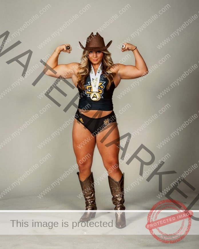 Kali Terza A muscular woman in a cowboy hat, sleeveless top, black shorts, and boots flexes her arms with a medal—celebrating.