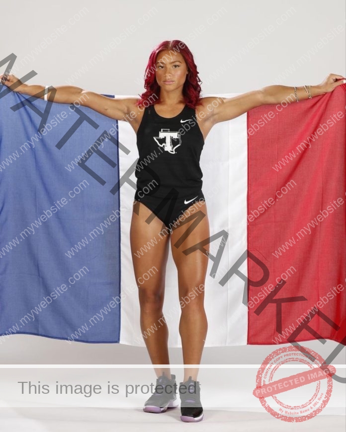 Aaliyah Rifort Delem Aaliyah Rifort Delem with striking red hair stands confidently holding a French flag, in black athletic wear and sneakers.