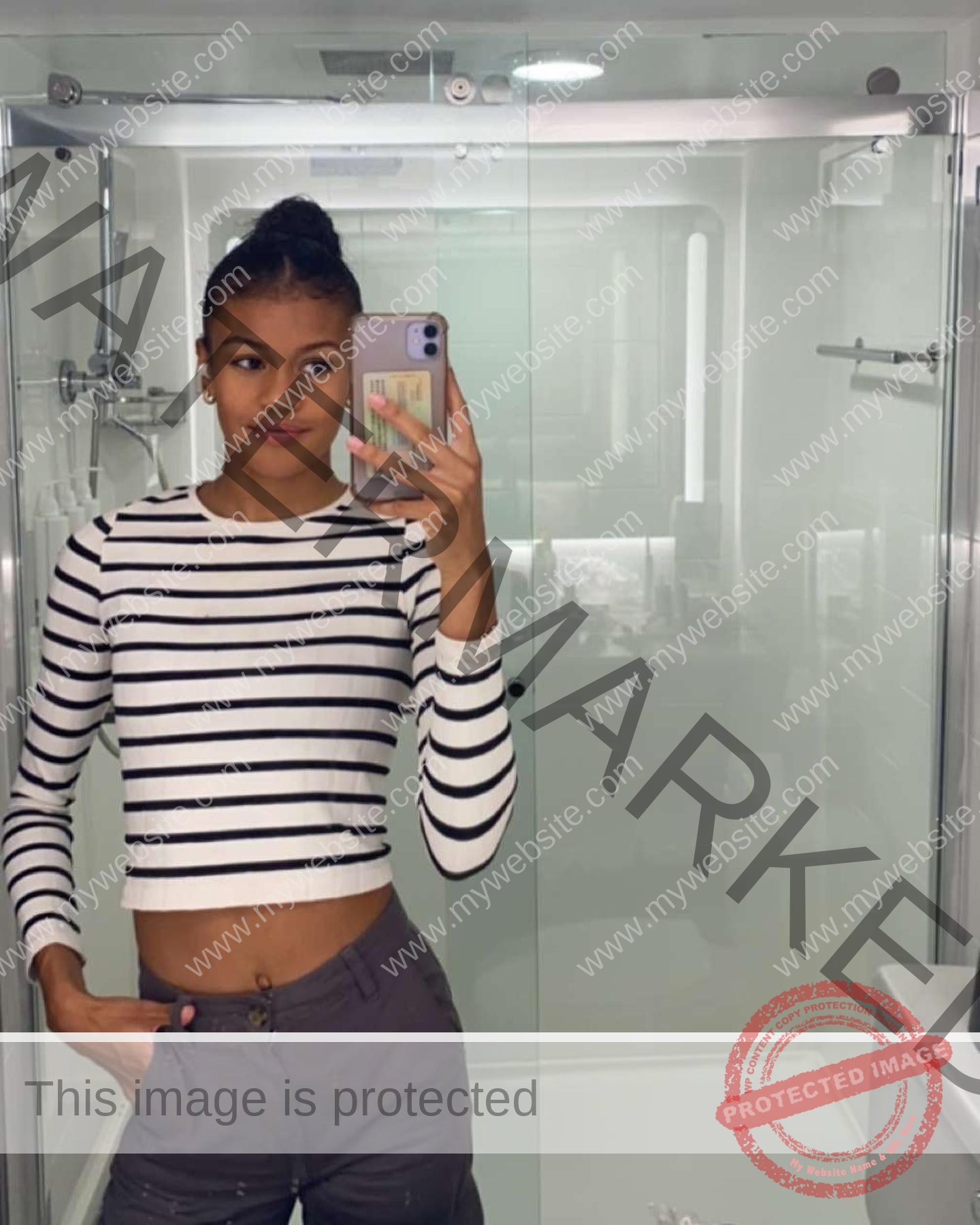 abigail-noruwa-netherlands-abigail_noruwa-u20-x-00020 Abigail Noruwa, track star from the Netherlands, wears a black and white striped crop top and gray pants, taking a mirror selfie in a modern bathroom with glass shower doors.