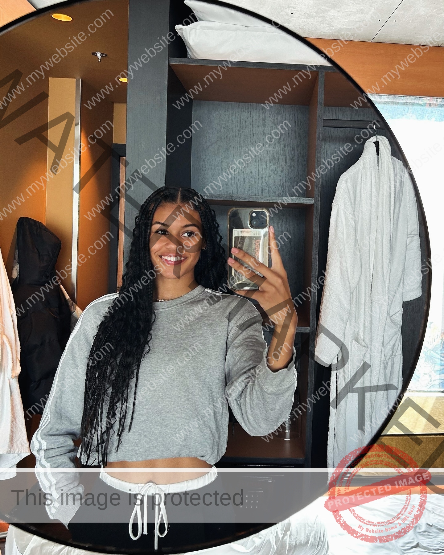 abigail-noruwa-netherlands-abigail_noruwa-u20-x-00042 Abigail Noruwa, track star from the Netherlands, takes a mirror selfie, smiling in a gray cropped sweatshirt and black pants.