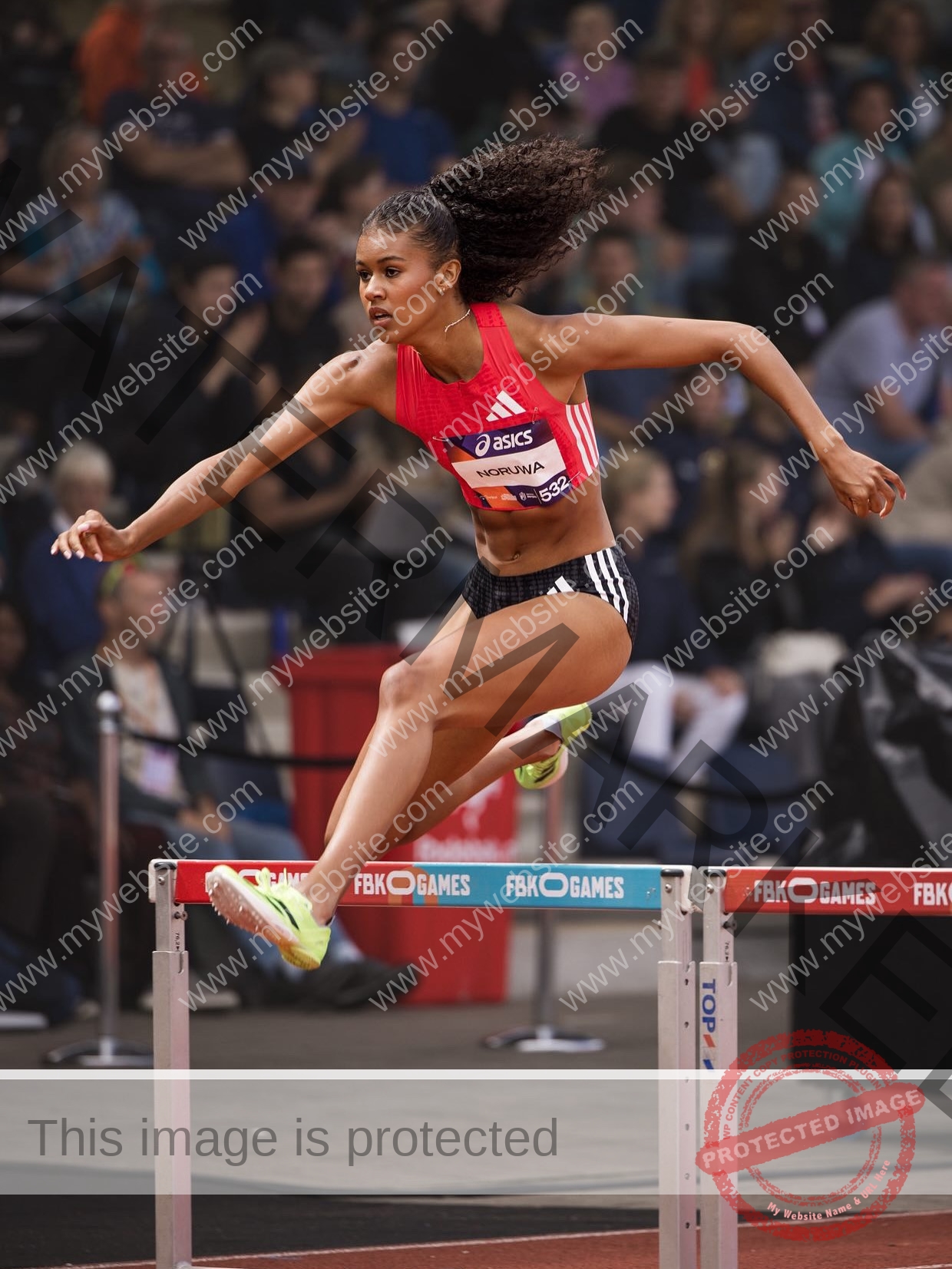 abigail-noruwa-netherlands-abigail_noruwa-u20-x-00087 Abigail Noruwa, track star from the Netherlands, in a red crop top and black shorts leaps over a hurdle in an indoor stadium race.