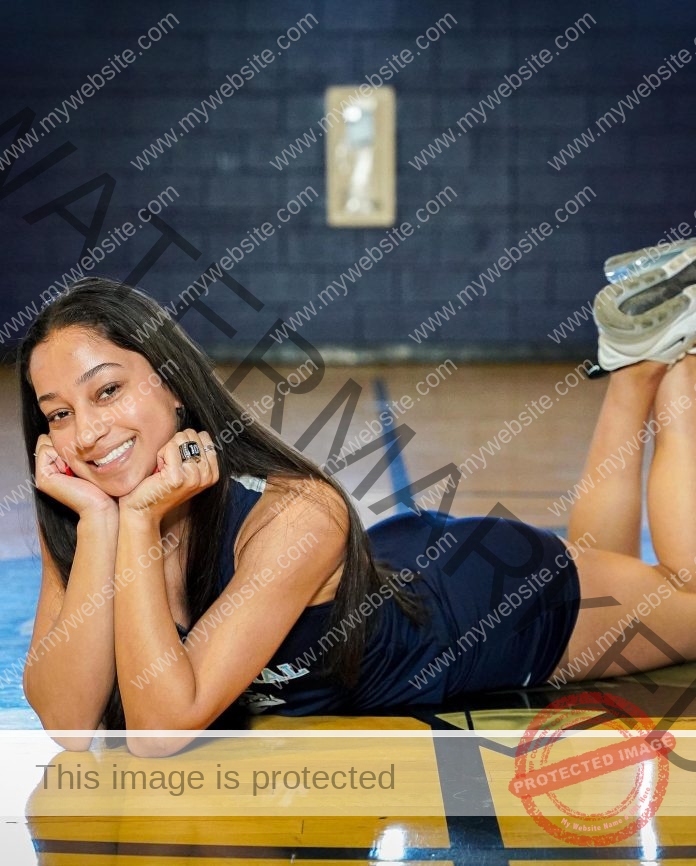 Adrian Powell A young woman in a navy Utah Valley athletic uniform lies on the gym floor, smiling with her chin on her hands, a ring visible.