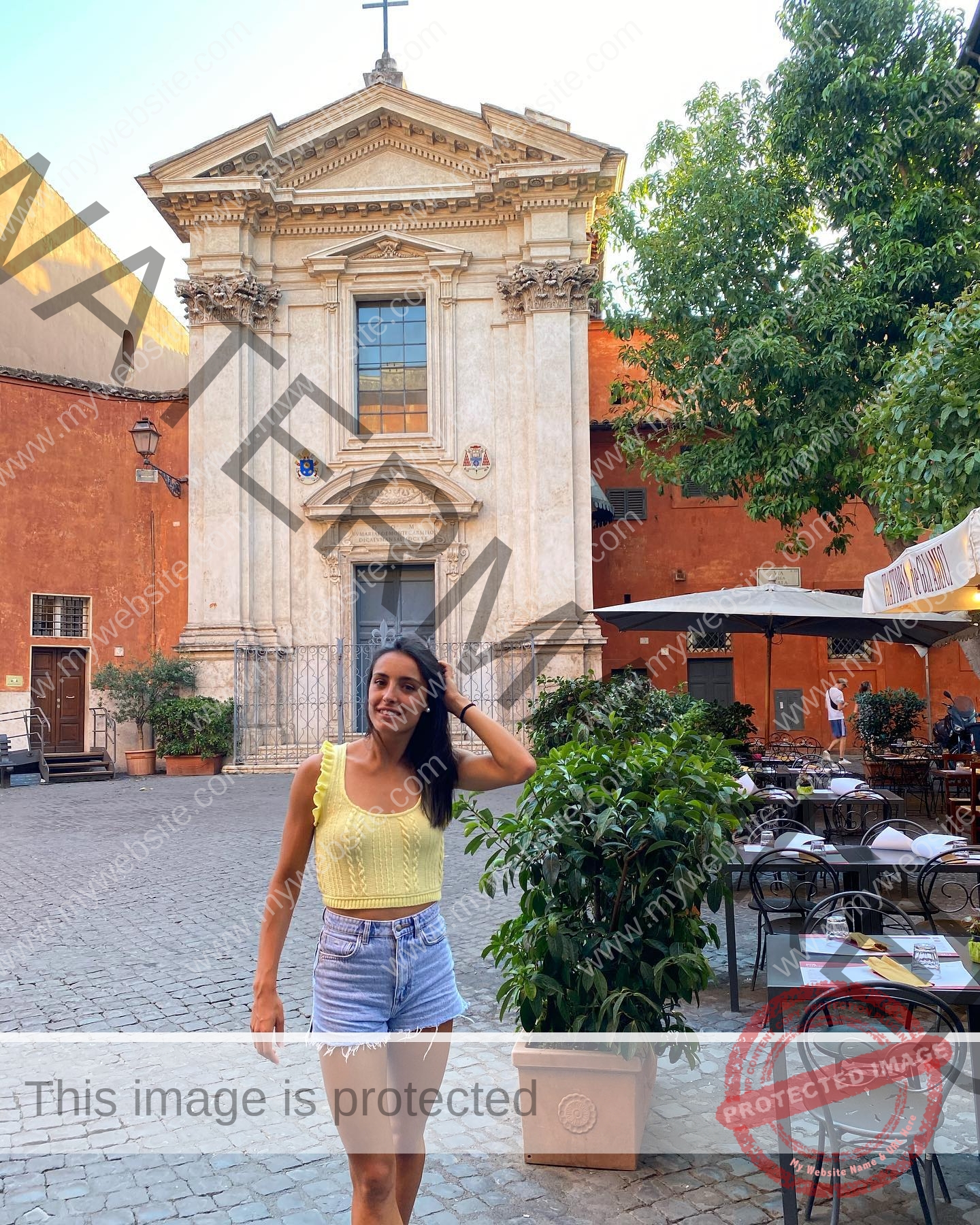 ainhoa-idoiaga-spain-ainhoidoiaga-00294 Ainhoa Idoiaga, track athlete from Spain, stands in a sunny cobblestone square in yellow top and shorts, smiling by a church.