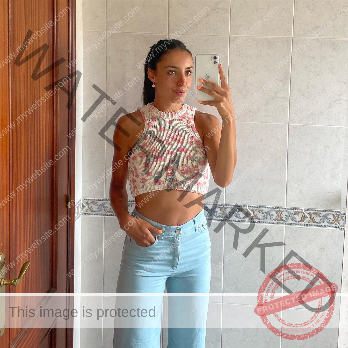 ainhoa-idoiaga-spain-ainhoidoiaga-00312 Ainhoa Idoiaga, track athlete from Spain, stands in front of a mirror taking a selfie in a floral crop top and blue jeans.